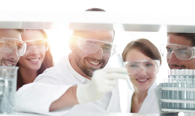 Grupo de químicos com óculos de proteção e luvas verificando tubos de amostras químicas.